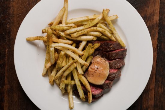 The bavette steak comes pink and glistening inside, and darkly crusty outside, smothered in skinny, skin-on fries.