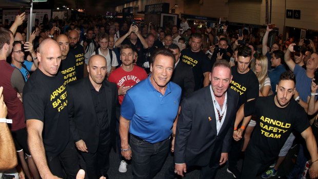 The "Arnold Safety Team" escorts the former strongman through Melbourne Exhibition Centre.