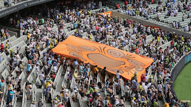 The national anthem takes place as an Indigenous mural is taken down the stand by fans.