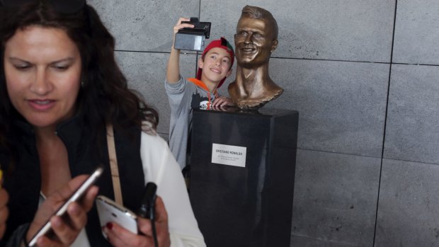 A boy takes a selfie next to the bust of Cristiano Ronaldo.