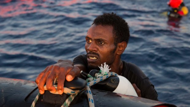 A migrant from Eritrea holds onto the side of a boat after jumping into the water from a crowded wooden boat during a rescue operation in the Mediterranean in August. 