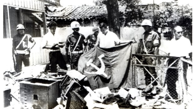 Indonesian police hold a communist flag in the ruins of Indonesian Communist Party  House in Jakarta after it was ransacked by anti-communist demonstrators in 1965.  