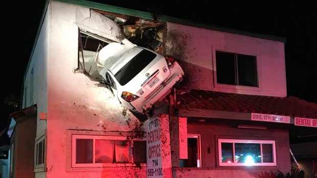 A car that crashed into a building in Santa Ana, California, hangs from a second storey window.