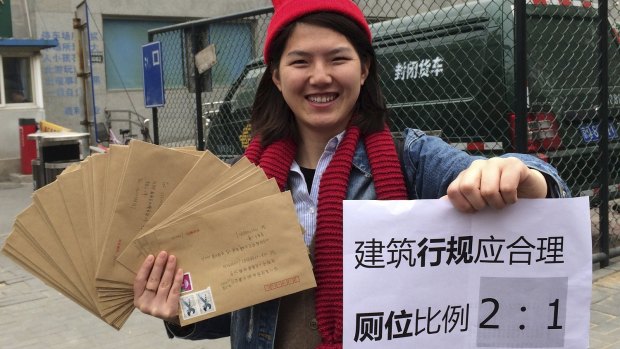 Female activist Li Tingting, 25, with a paper that reads "Construction regulations should be reasonable, bathroom proportion 2:1 (women/men)".