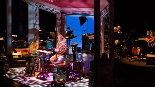 On stage: Merritt is encased with various instruments in a doll's house-like box, with the band behind.