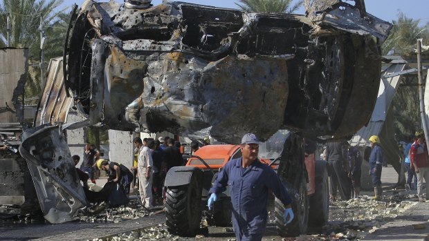 War still evident in Iraq: Civilians and security forces gather as municipality workers remove destroyed vehicles at the scene of a deadly suicide bomb attack in Hillah, about 95 kilometres south of Baghdad. 