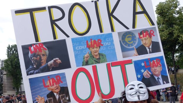 A man holds a sign that reads "Troika Out"  in Paris. 