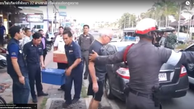 An elderly bridge player is arrested by a Thai policeman in Pattaya.