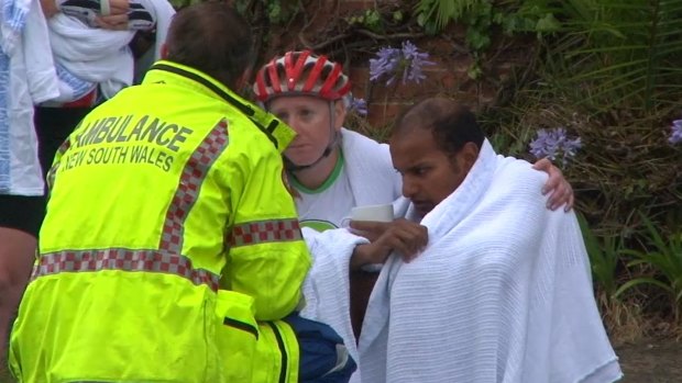 An ambulance officer comforts cyclists after a woman was killed on Mona Vale Road, Pymble.