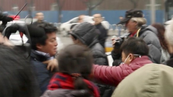 A plain-clothes policeman (in red jacket) seizes Fairfax Media's China Correspondent Philip Wen outside the courthouse.