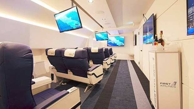 Grounded travellers sit in first or business class seats in a mock airline cabin where they are served in-flight meals and drinks, with flat panel screens displaying aircraft exterior views including passing clouds.