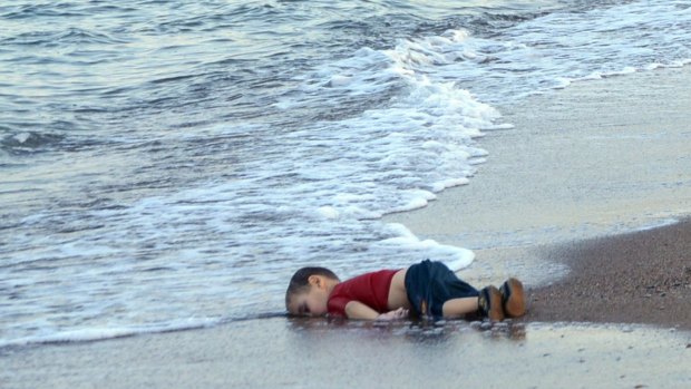 The lifeless body of an unidentified boy lies on a Turkish beach in front of paramilitary police officers.