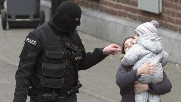Police evacuate a woman and a small child during a police raid targeting Paris attacks suspect Salah Abdeslam.