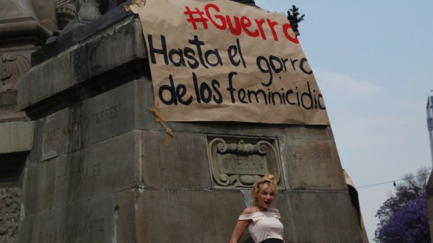 A woman poses under a sign that reads in Spanish: "Guerro (white men) up to their necks in femicide," before the start of a march in Mexico.