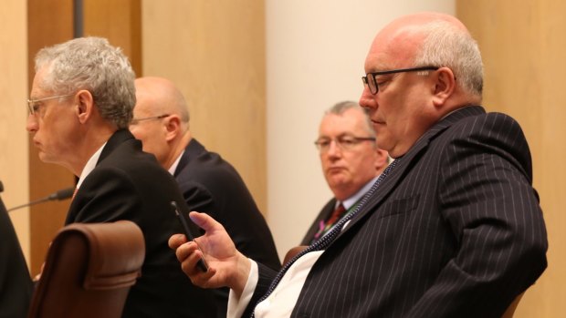Attorney-General Senator George Brandis (right) checks his phone during the Senate budget estimates hearing with PM&C officials at Parliament House on Monday.
