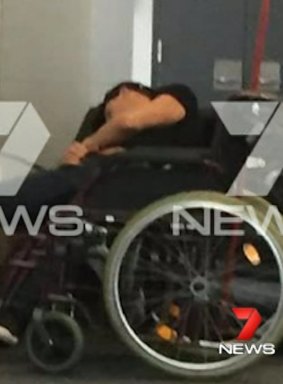 The man appears to be slumped over on airport seats next to a wheelchair.