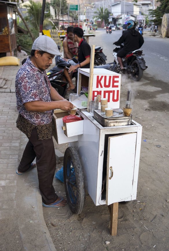 Food cart Kue Putu arrives at dusk selling steamed pandan rice cakes.