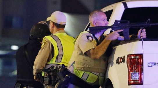 A police officer takes cover behind a truck. 