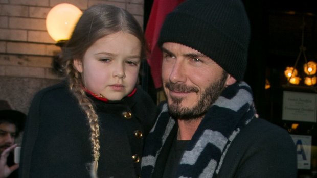 A sombre-looking Harper Beckham is carried by father David at her mother's fashion show in New York last weekend.