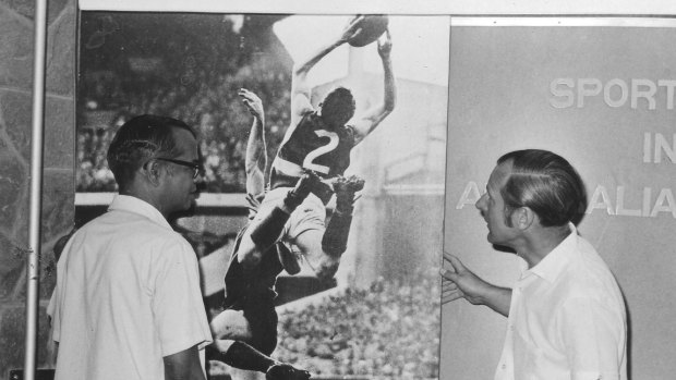 Rex Scambary (right) did a good job of describing Australian Rules to Indian visitors at a sports exhibition at the High Commission in New Delhi. The poster shows Footscray rover Merv Hobbs' famous mark in the 1961 preliminary final.