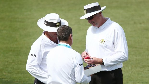 The umpires discuss the state of the ball.