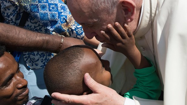 Pope Francis caresses a child as he meets with migrants at his weekly general audience in St Peter's Square at the Vatican.