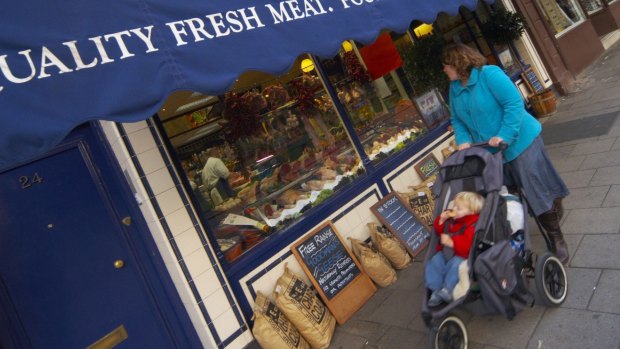 A mother pushes her baby in a pram past a butchers at the vintage markets of London.  