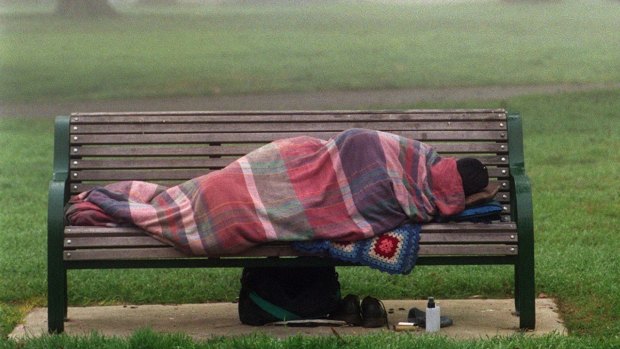 A homeless person lies bundled on a park bench in the Fitzroy Gardens, East Melbourne, as a freezing fog began to lift.