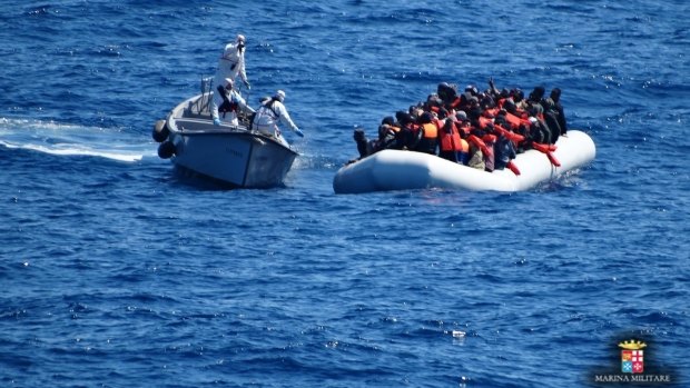 Italian navy personnel, left, approach a rubber dinghy filled with migrants in the Sicilian Channel on Friday.
