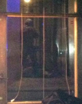 A policeman stands next to a person lying on the ground outside a synagogue in Copenhagen, viewed from inside a cafe across the street.