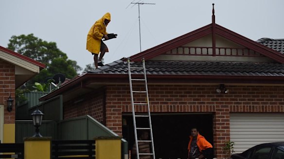A man removes damaged tiles from the roof of a home on Methven Street in Mount Druitt.