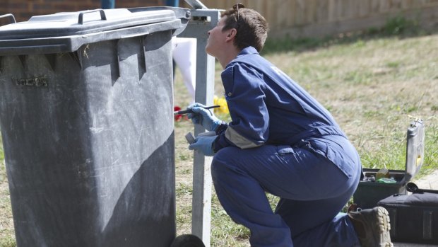 A forensics police officer dusts a bin that sits near the scene were the teenager was stabbed to death.