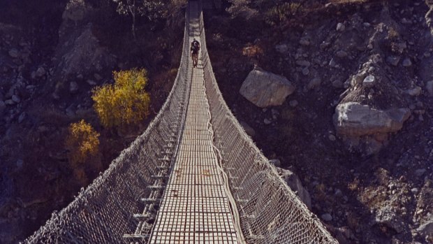 Trekkers crossing wire rope suspension bridge over Kali Gandaki river at Ghasa on Annapurna circuit Himalayas Nepal.
