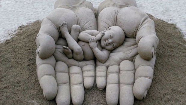 Hands holding a baby, sand sculptor by Dennis Massoud in the Canary Islands.
