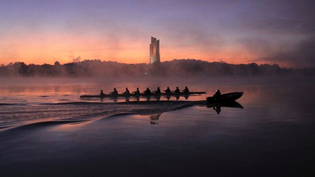 Rowers glide through mist on Lake Burley Griffin. 
