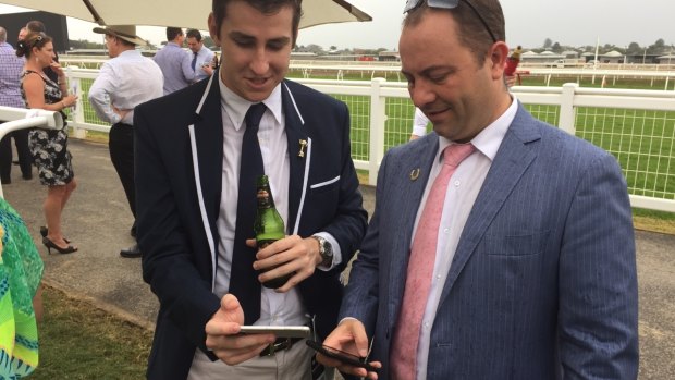 Zac and Leon Cleal watch the Melbourne Cup on their phones at Eagle Farm Racecourse after a blackout.