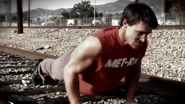 A screenshot from a Greg Plitt fitness video showing him working out on train tracks.