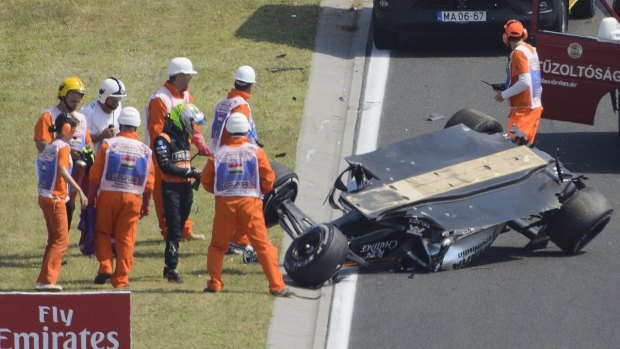 Force India driver Sergio Perez of Mexico, green helmet,  stands next to his overturned car.