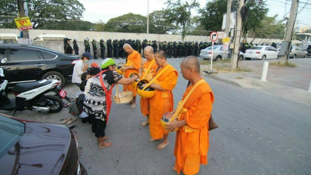 Monks at Thailand's largest Buddhist temple Wat Dhammakaya accept an offering while police line up in the background.