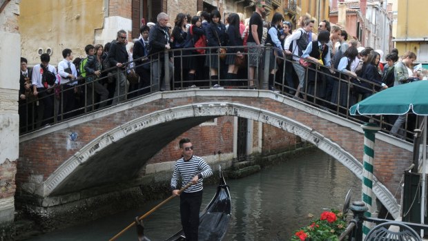 A crowd of tourists cross a bridge in Venice.