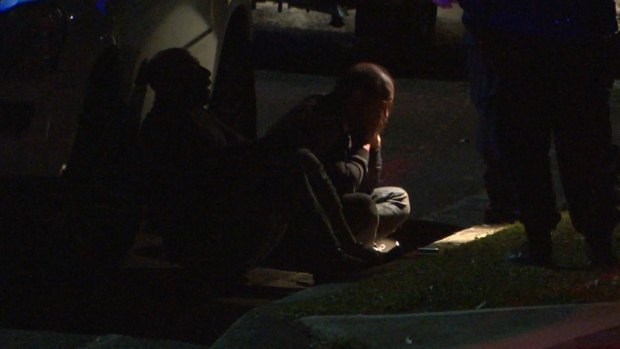 Two men sit in the gutter after a girl was shot dead in Lalor Park.