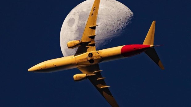 A Qantas 737 passes the moon at sunset.
