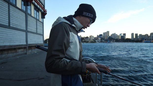 Eddie Yin, 24, tries to keep warm while fishing at Walsh Bay in Sydney on Wednesday morning.