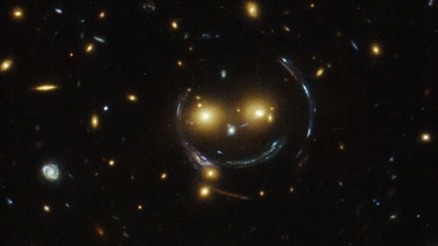 In the center of this image, taken with the Hubble Space Telescope, is the galaxy cluster SDSS J1038+4849 — and it seems to be smiling.