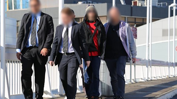 Police officers escort Moudasser Taleb (in red) out of Sydney Airport.