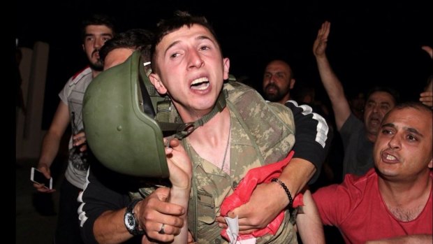 A Turkish soldier being held by members of the public. 