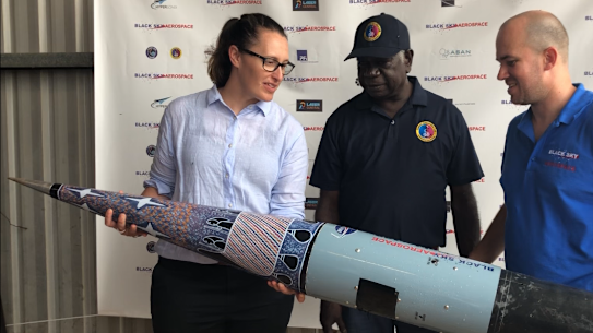 From left to right: Carley Scott, chief executive of ELA, Djawa Yunupingu, traditional owner, from Gumatj Corporation, Blake Nikolic, chief executive of ELA customer Black Sky Aerospace. Painting on the cone of the rocket by painting by artist Dorothy Djakangu Yunupingu. 