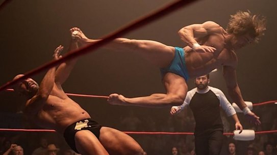 Zac Efron (right), as Kevin Von Erich, launches himself at an opponent in the wrestling ring in The Iron Claw.