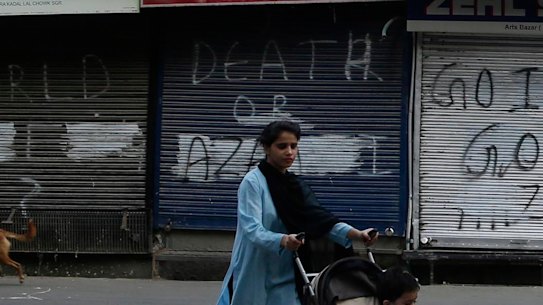 A Kashmiri woman pushes a child on a stroller past a closed market in Srinagar, Indian controlled Kashmir on Tuesday.