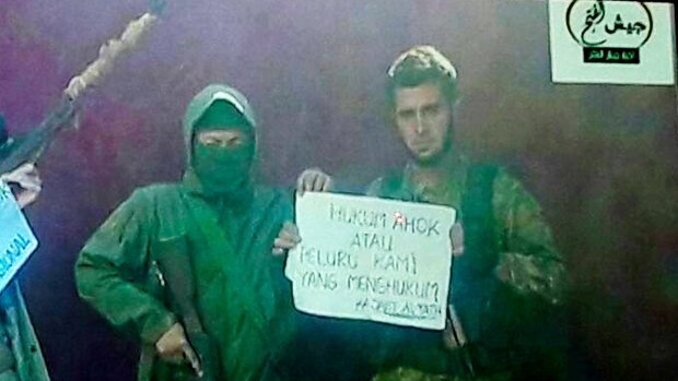 Member of a Syrian jihadist group hold a sign that reads "Punish [Jakarta governor] Ahok or our bullets will."